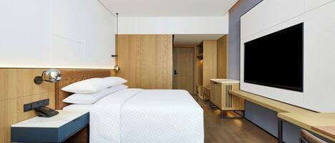 A modern hotel room with a large bed, a desk, a flat-screen TV, and a small seating area.