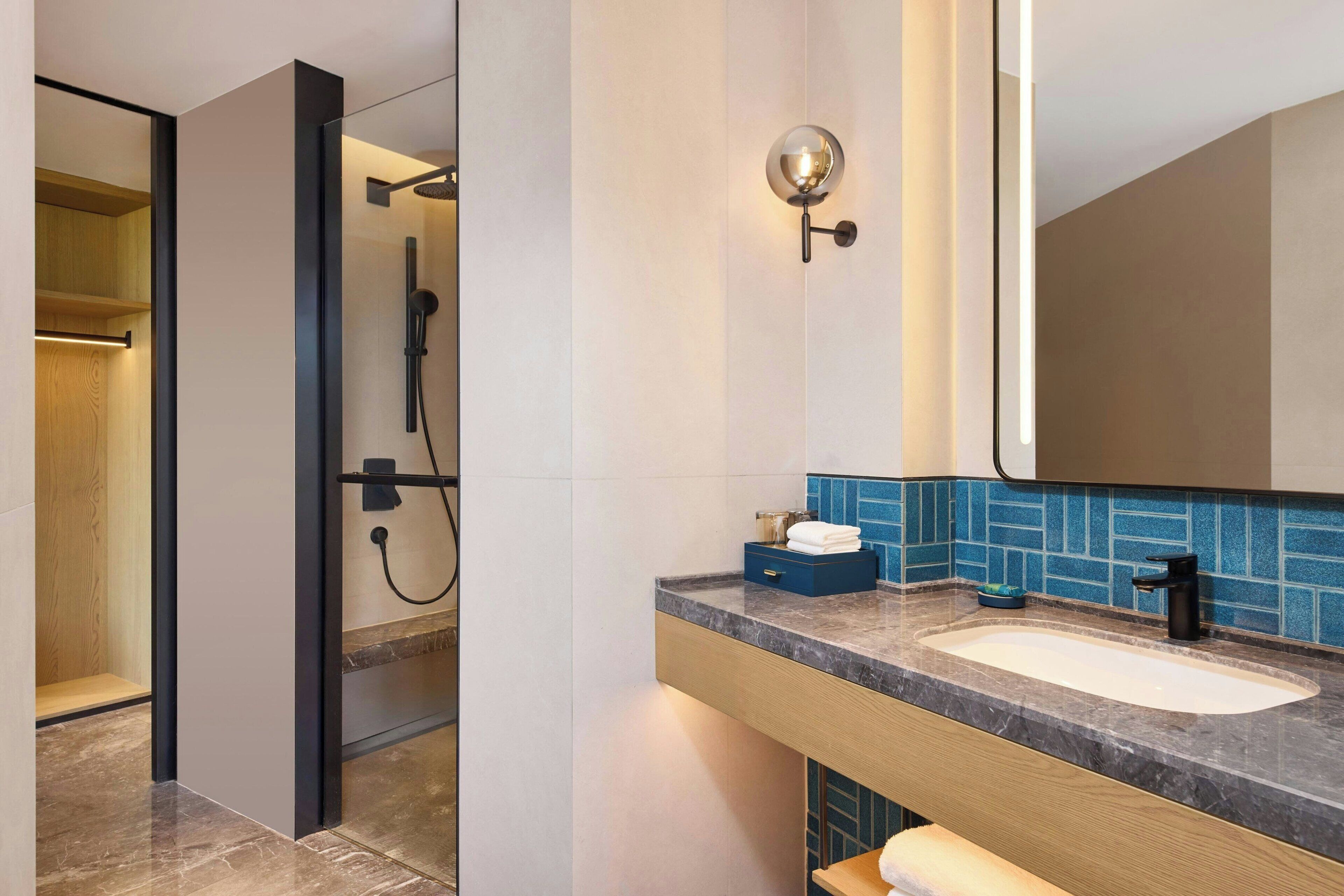A modern bathroom with a glass-enclosed shower, a marble sink, and a blue-tiled backsplash.