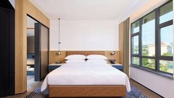 A modern hotel room with a large bed, wooden headboard, and a view through floor-to-ceiling windows.