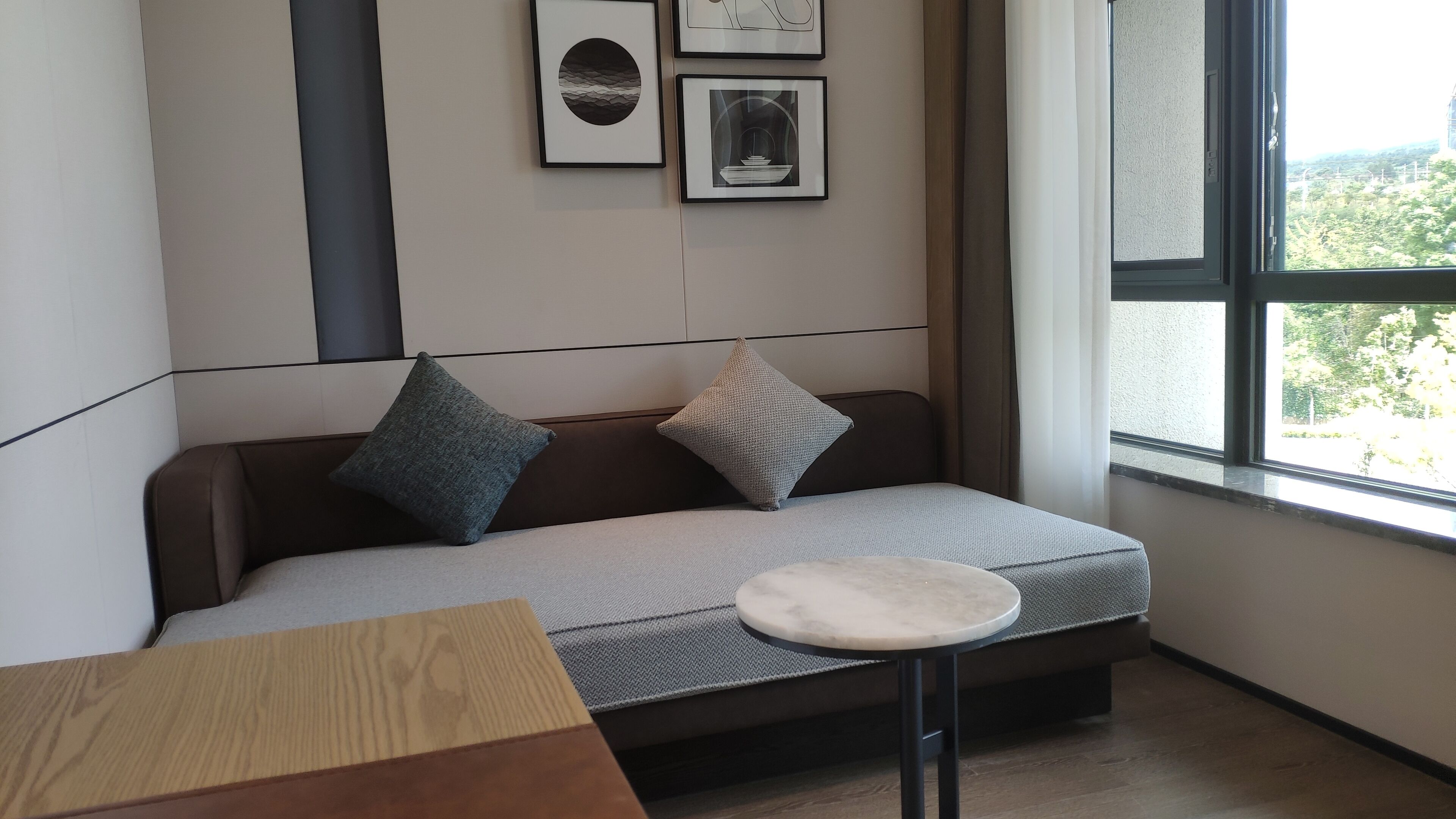 Una habitación moderna con un sofá gris, dos almohadas, una mesita redonda y cuadros en la pared.
