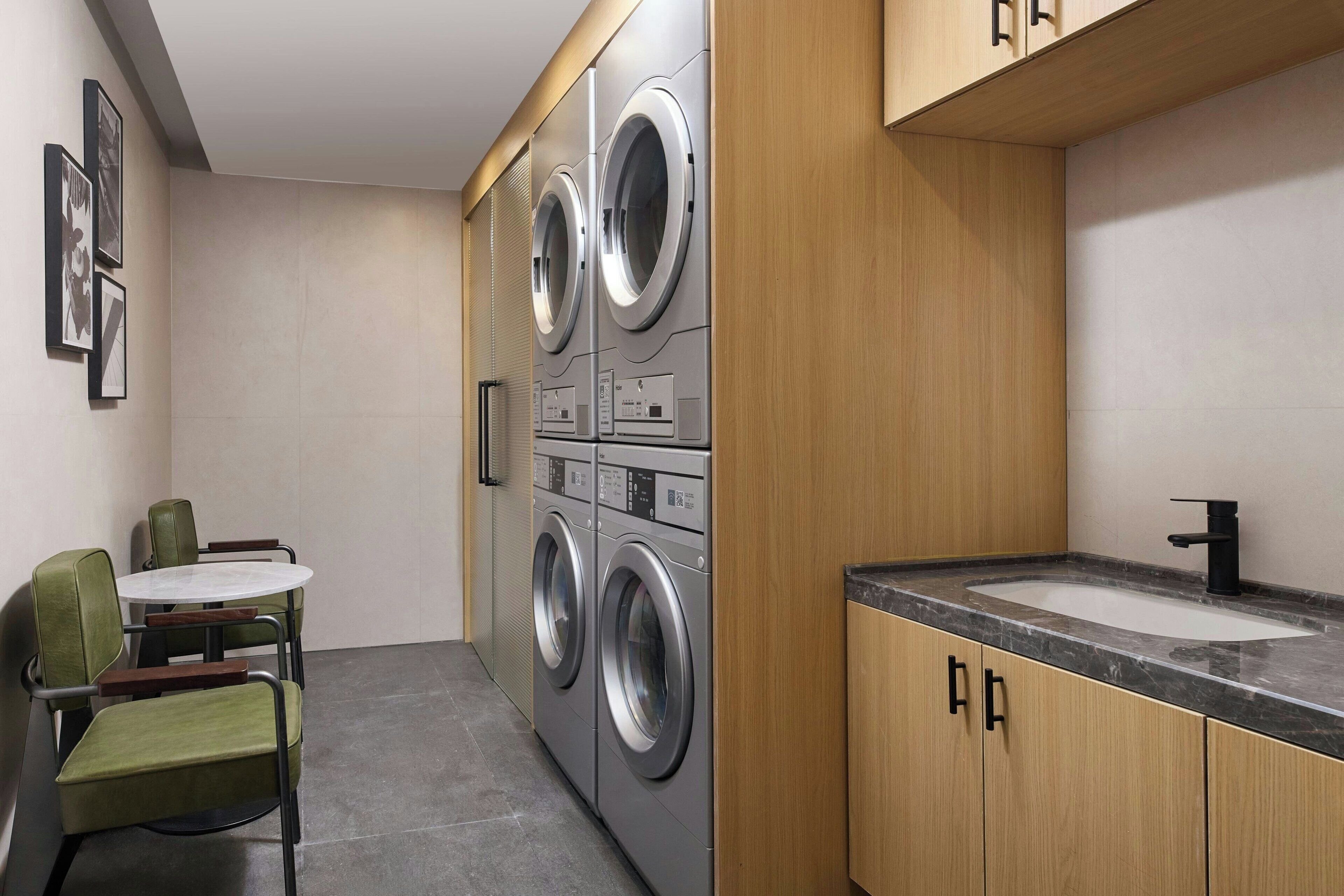 A compact laundry room with a washing machine, a sink, and a small table with chairs.