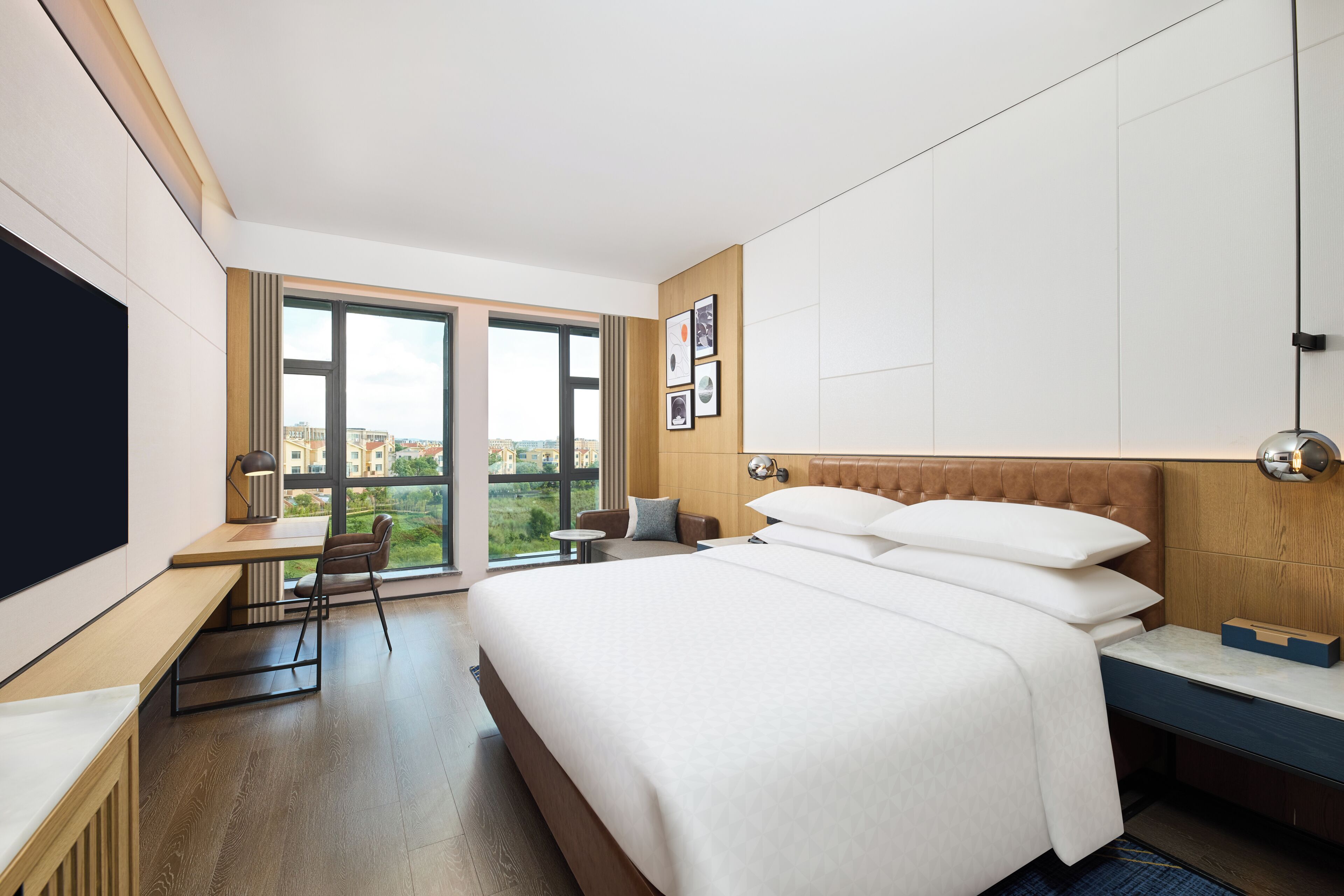 A hotel room with a large bed, a desk with a chair, a TV, and a window with a city view.