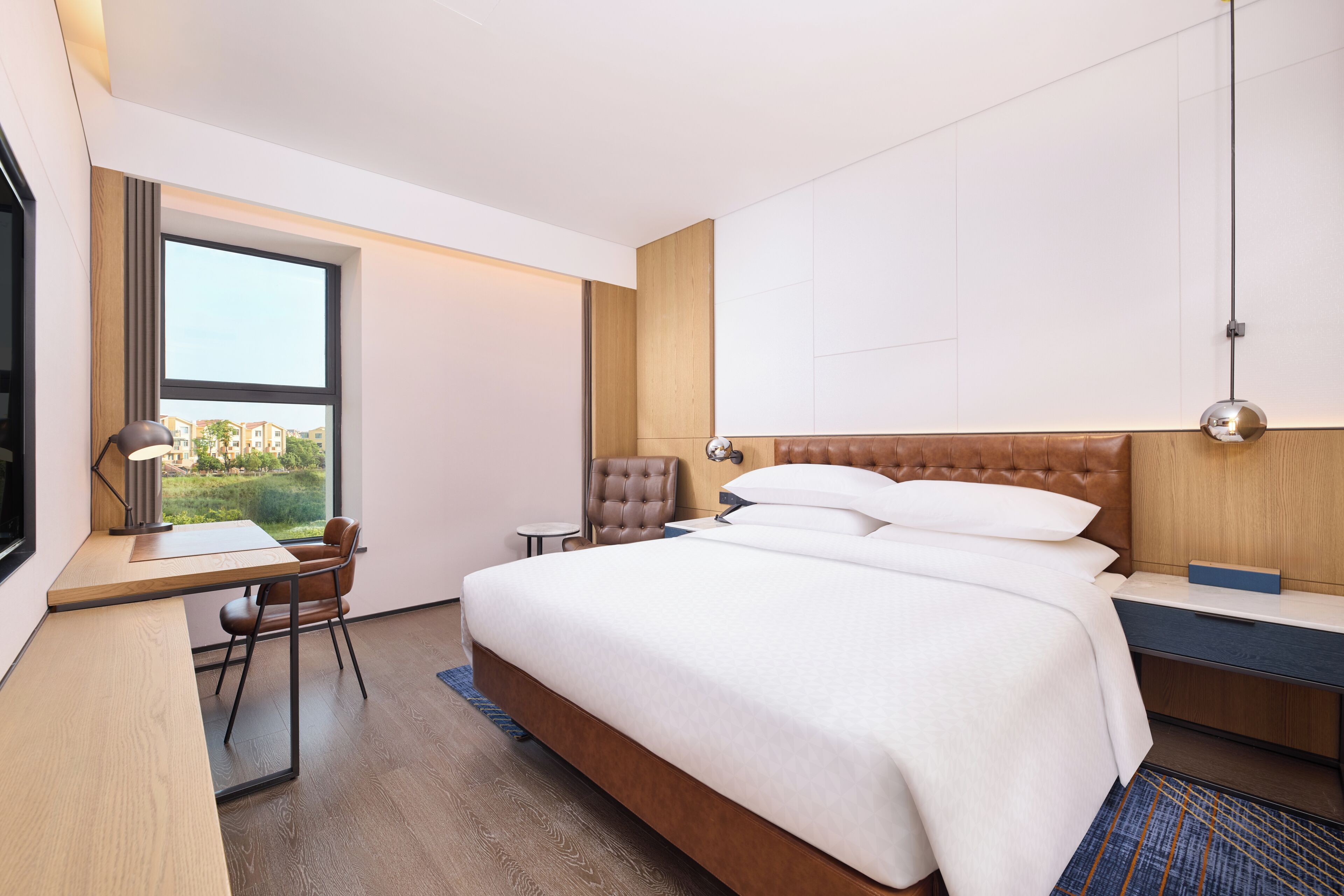 Habitación de hotel moderna con una cama grande, un escritorio, una silla y vistas al exterior.