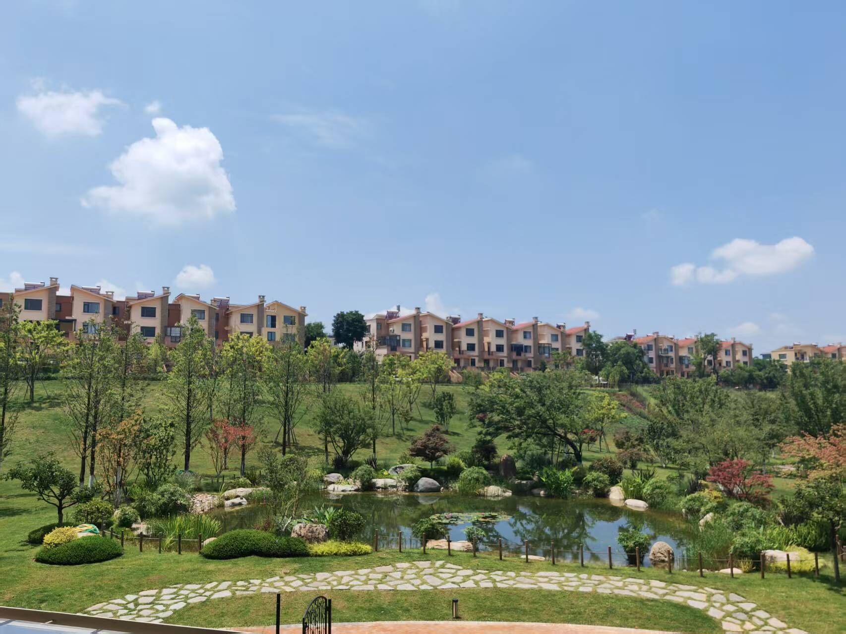 A residential complex with multiple apartment buildings, a well-maintained garden with a pond, and a stone pathway.
