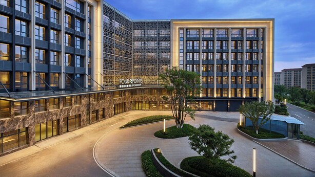 A modern hotel with a glass facade, a well-lit entrance, and a landscaped courtyard.