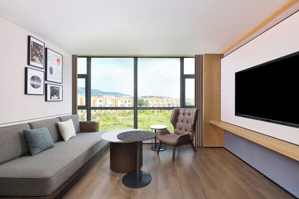 Una sala de estar moderna con un sofá, una mesa redonda, una silla y un ventanal con vistas a la ciudad.