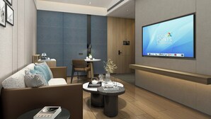 Een moderne hotellobby met een groot scherm waarop "FOUR POINTS BY SHERATON" staat, een bank, een salontafel en een eetgedeelte.