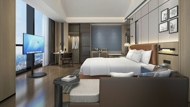 Een moderne hotelkamer met een groot bed, een bureau met stoel, een televisie en uitzicht op de stad.