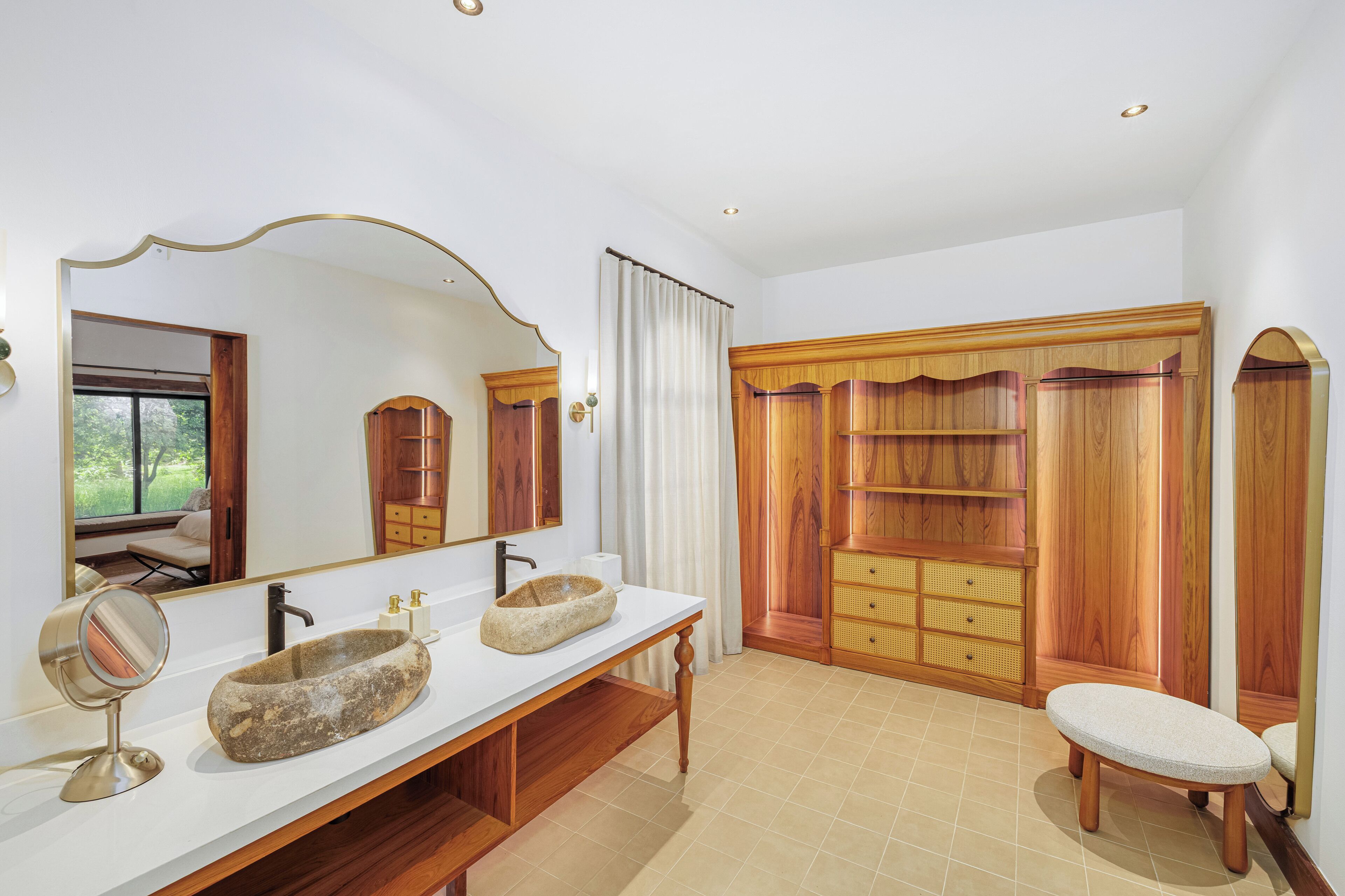 Ein Badezimmer mit einem Doppelwaschbecken, einem großen Spiegel, Holzschränken und einer Sitzbank.
