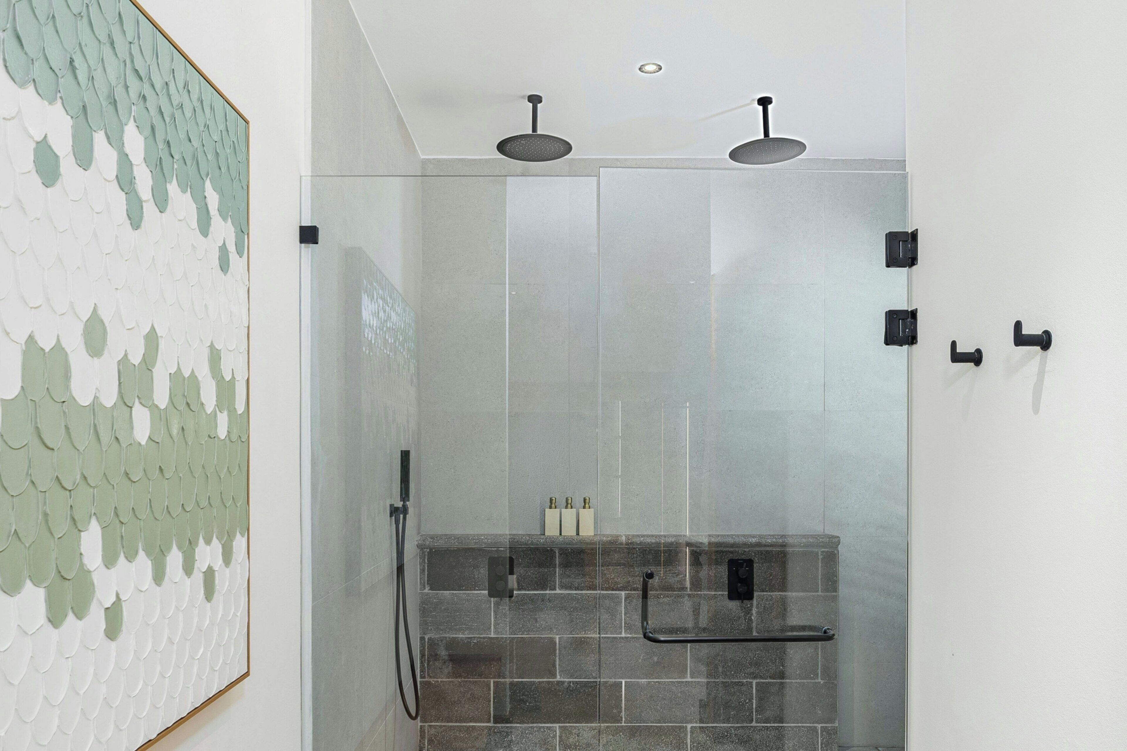 A modern shower with a glass door, a tiled wall, and a framed artwork on the left.