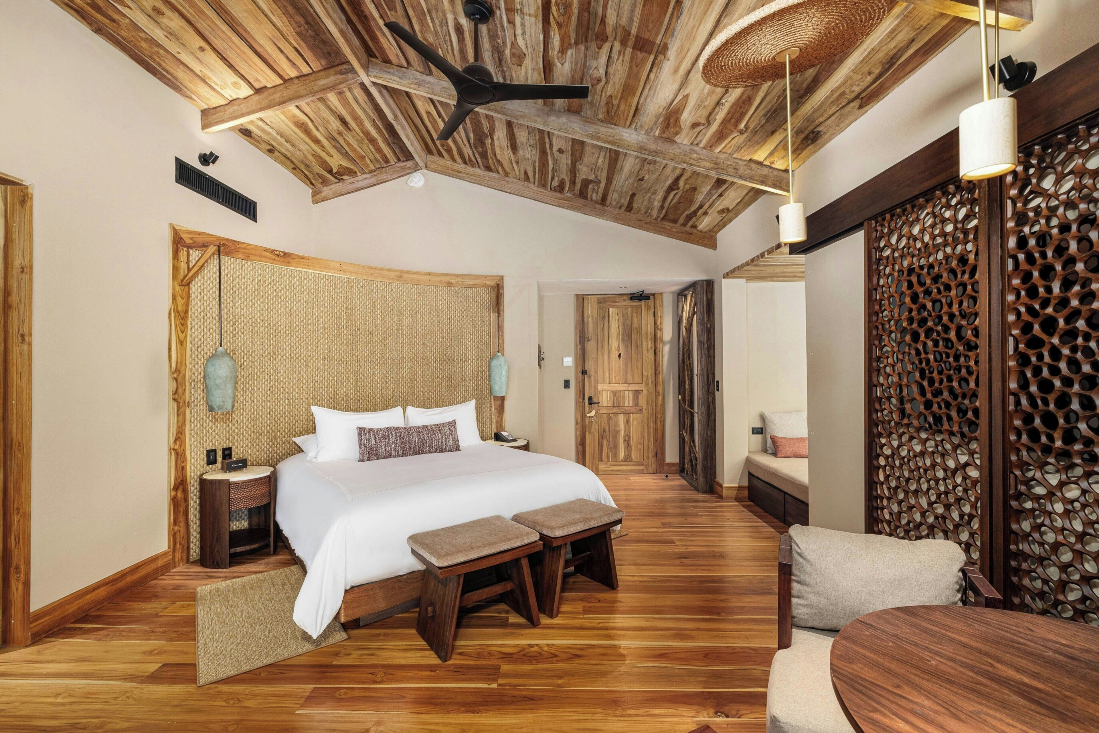 A spacious bedroom with a large bed, wooden flooring, a ceiling fan, and a wooden partition wall.