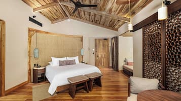 A spacious bedroom with a large bed, wooden flooring, a ceiling fan, and a wooden partition wall.