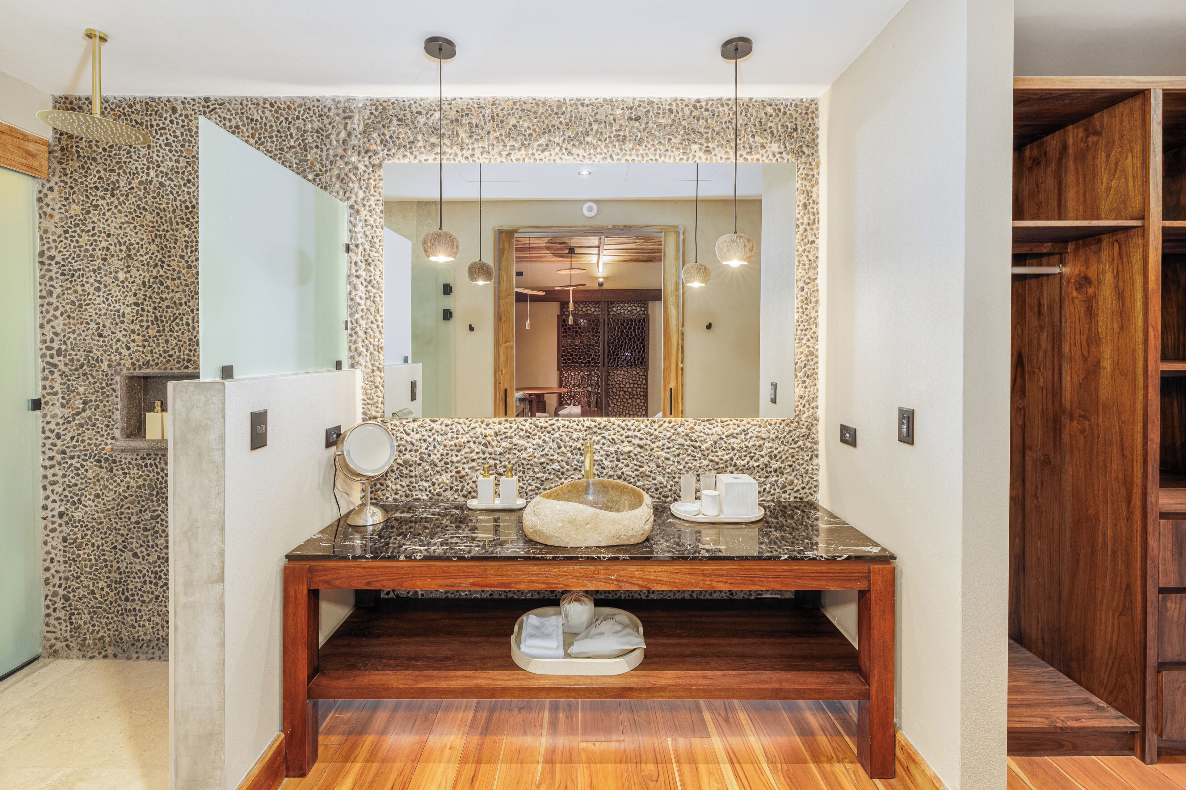 Un baño con pared de piedra, tocador de madera, espejo grande y piso de madera.