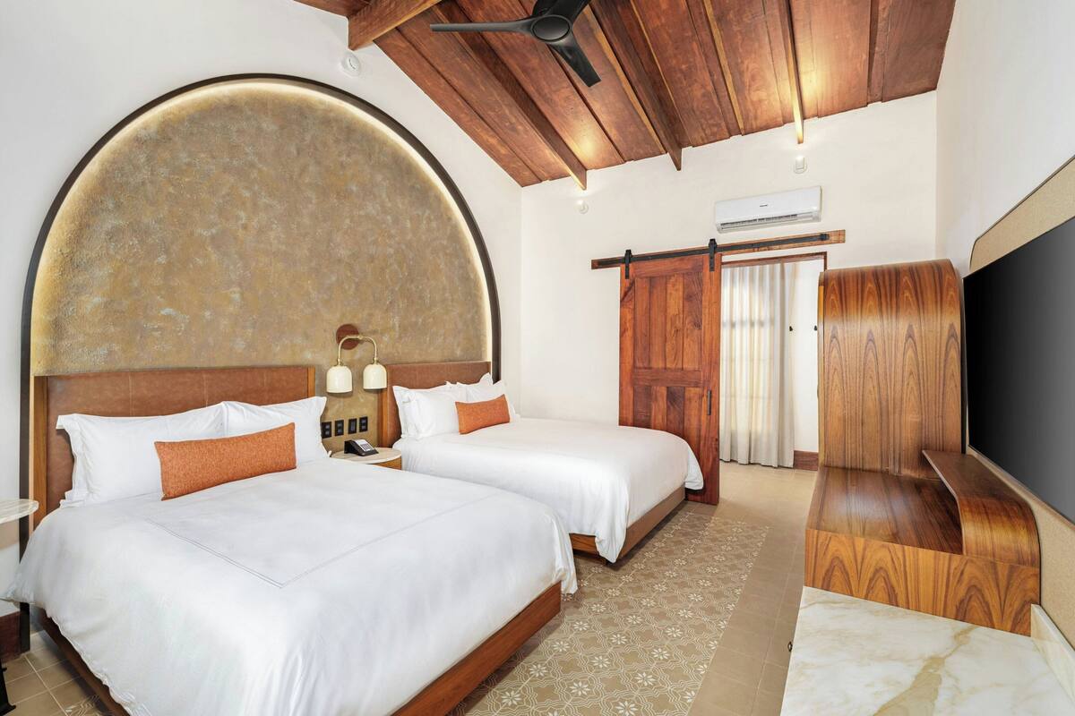 Quarto de hotel com duas camas, uma parede curva grande, teto de madeira e uma televisão.