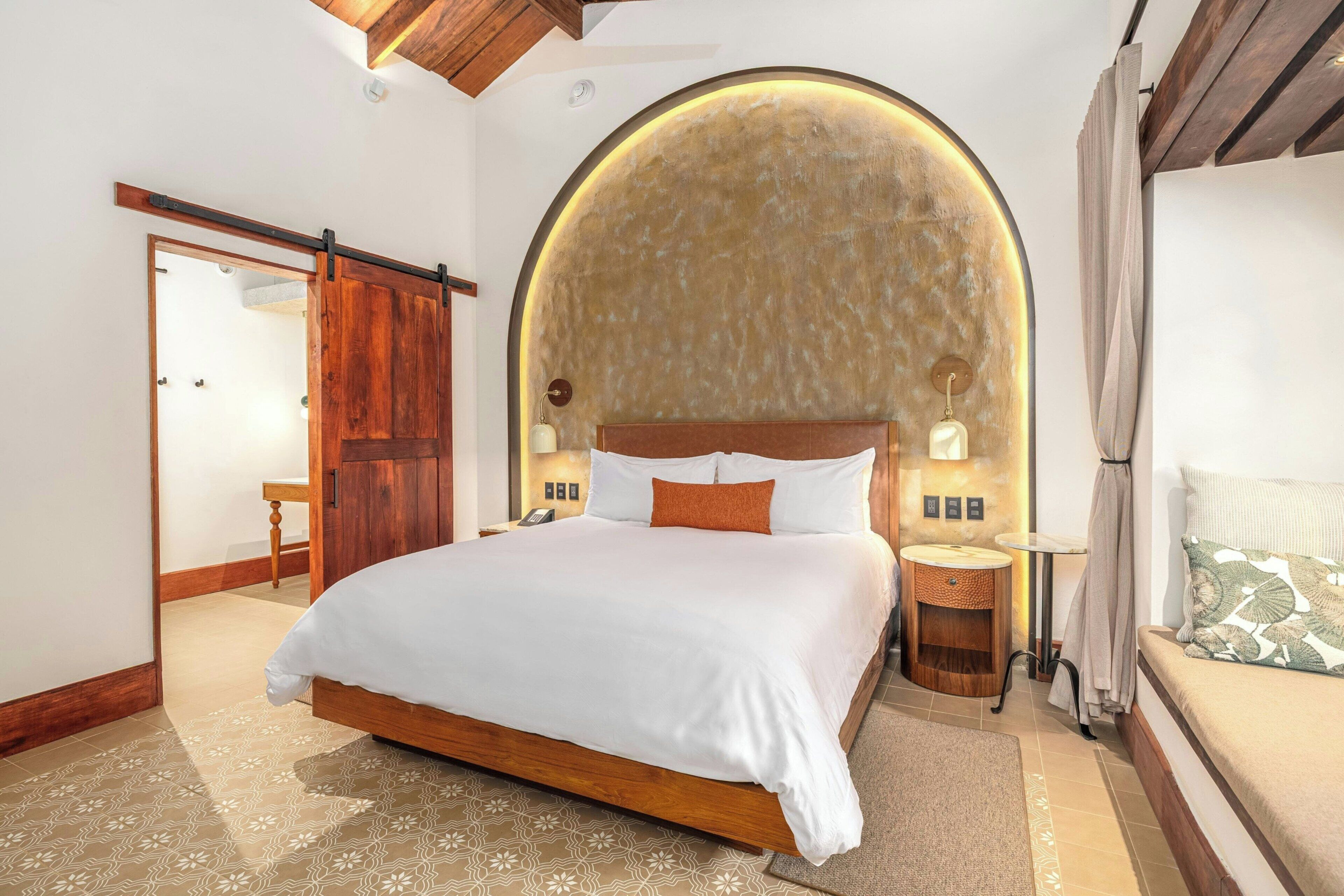 Une chambre avec un grand lit, une tête de lit en bois, un élément décoratif rond au mur, une table de chevet et une petite table ronde.