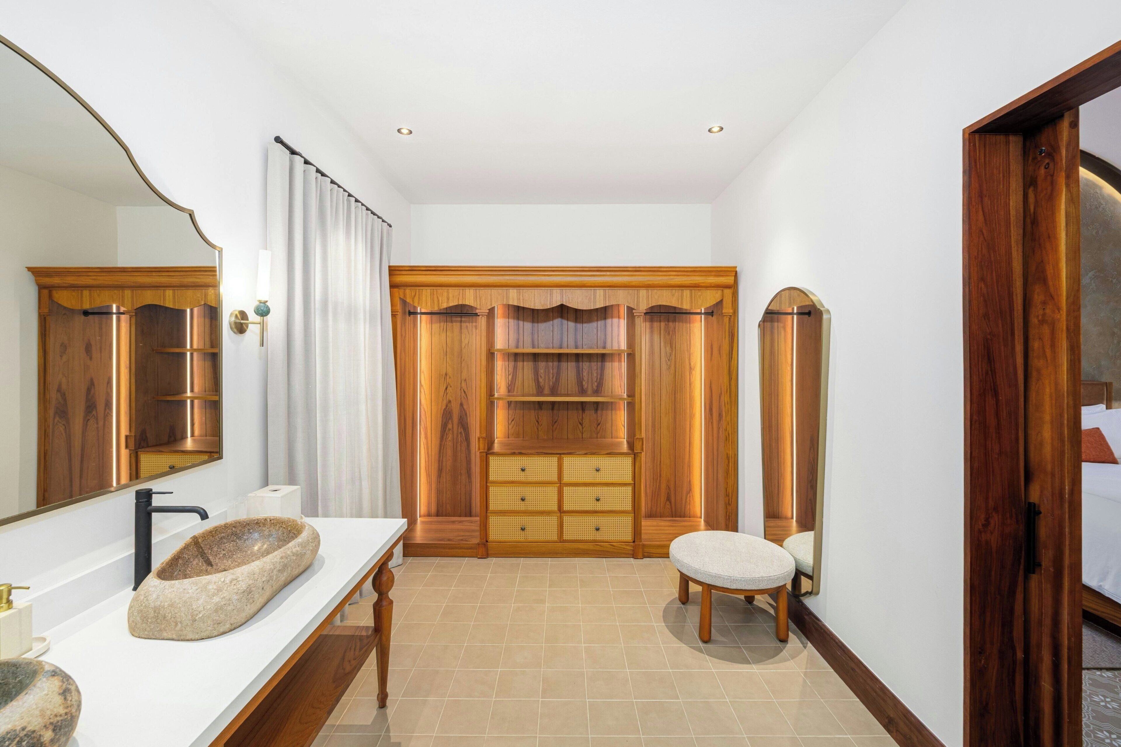 Un baño con lavamanos de piedra, tocador de madera y un espejo grande.