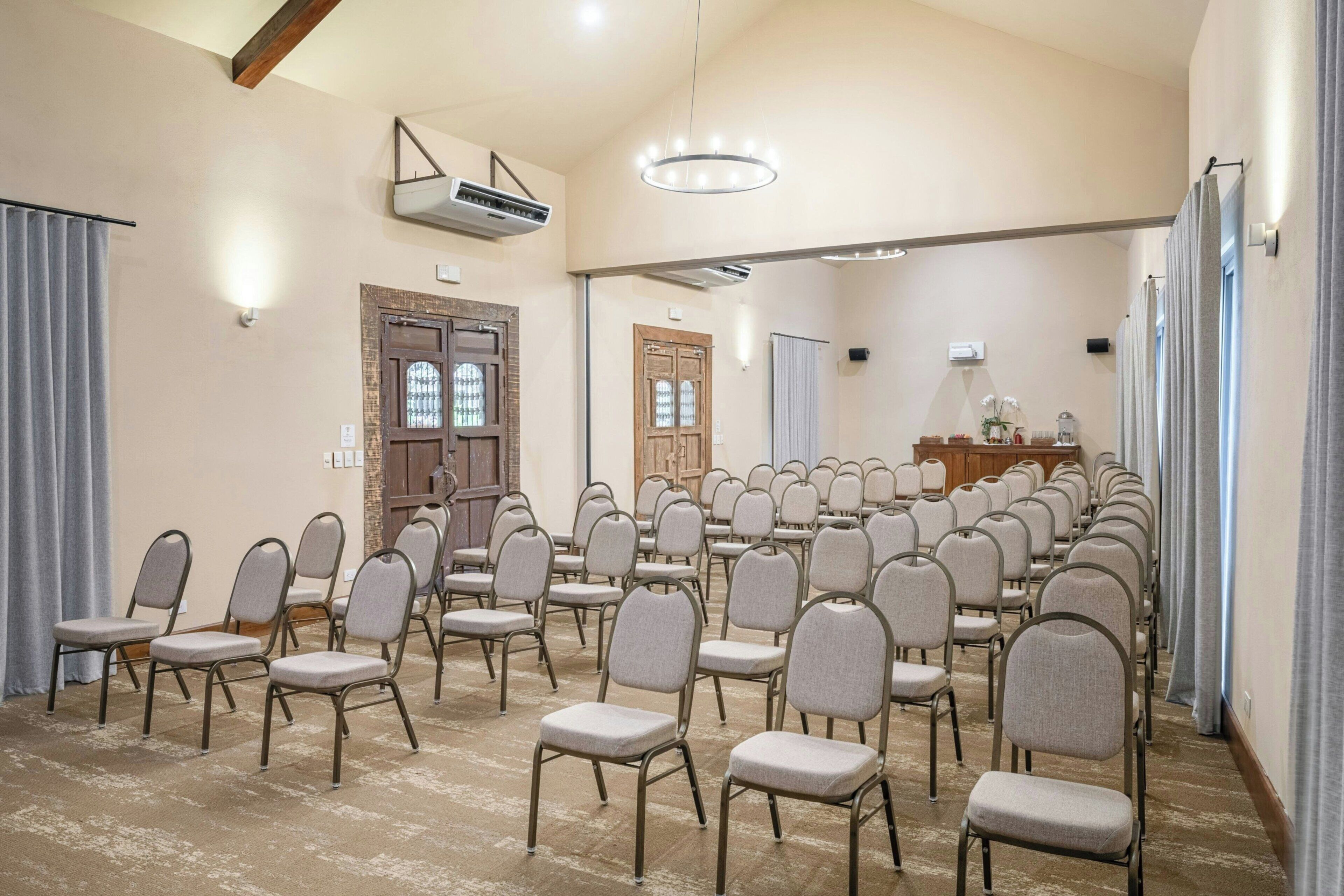 Une salle de conférence avec des rangées de chaises, un appareil de climatisation, un lustre et une porte en bois dotée de panneaux de verre.