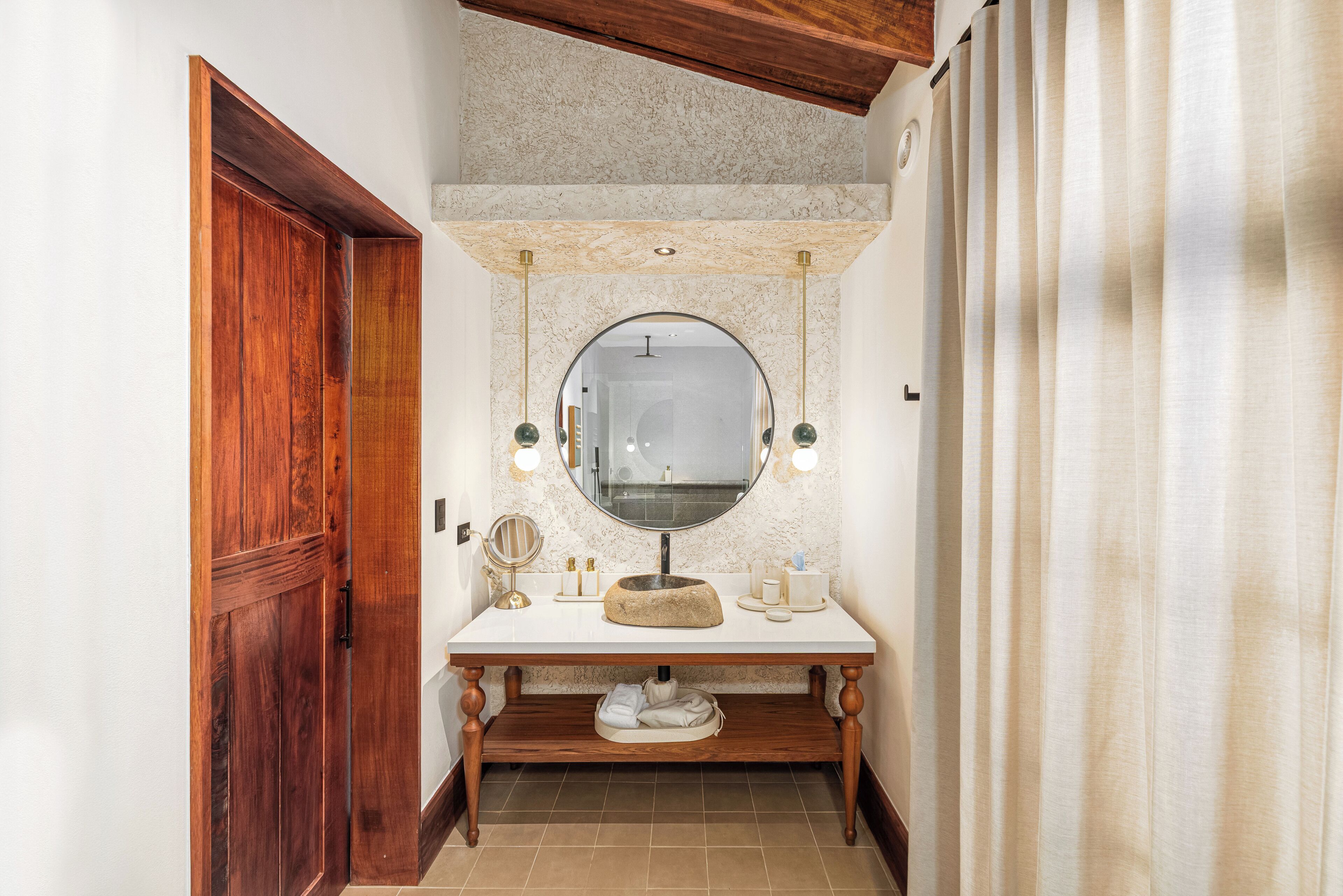 A bathroom with a wooden door, a marble sink, a round mirror, and a towel rack.