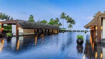 Ein ruhiger Infinity-Pool mit einer Holzkonstruktion an einer Seite und Blick auf Palmen.