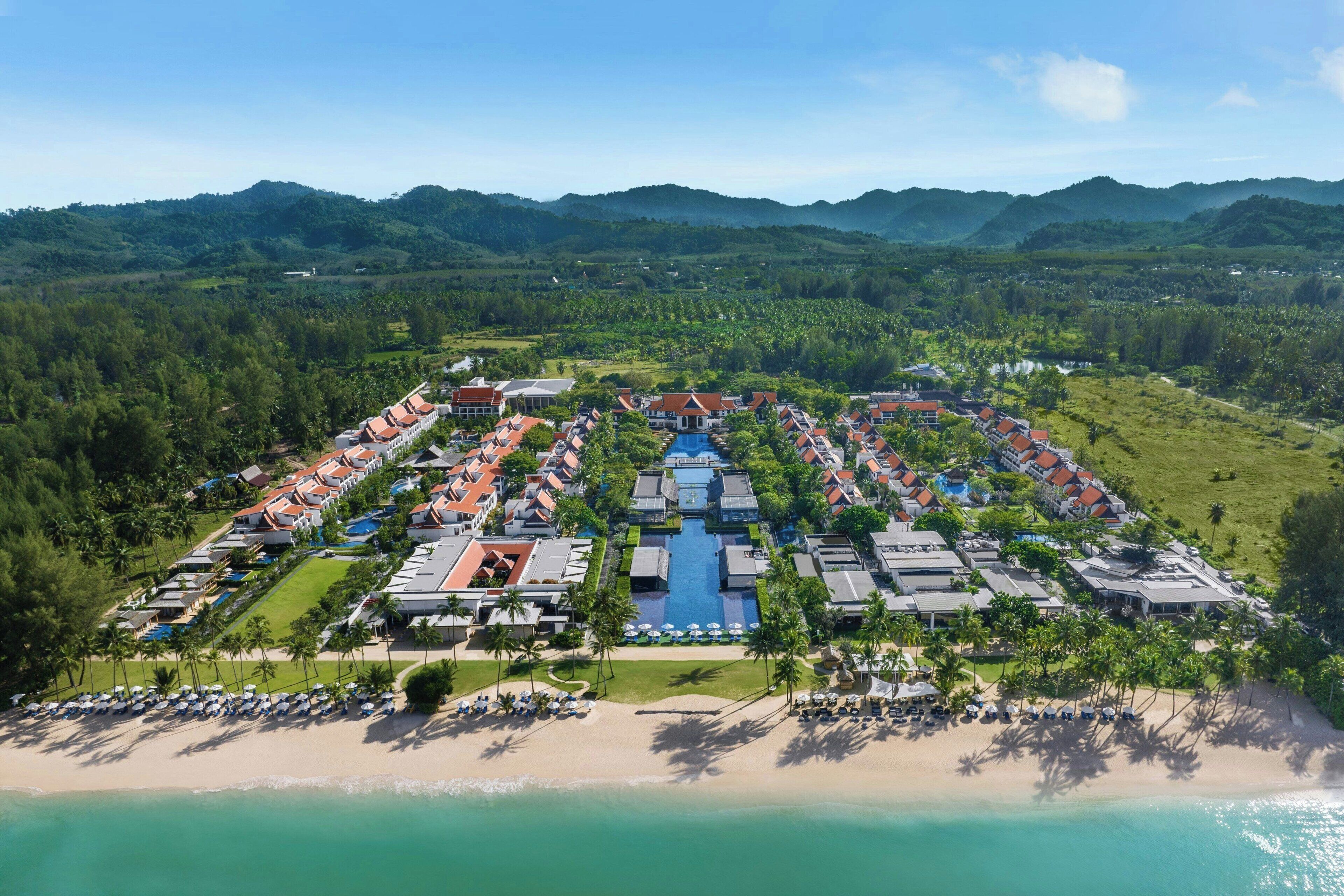 An aerial view of a resort with multiple buildings, a central pool, and a beachfront.