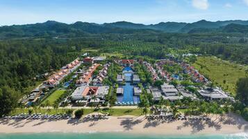 An aerial view of a resort with multiple buildings, a central pool, and a beachfront.