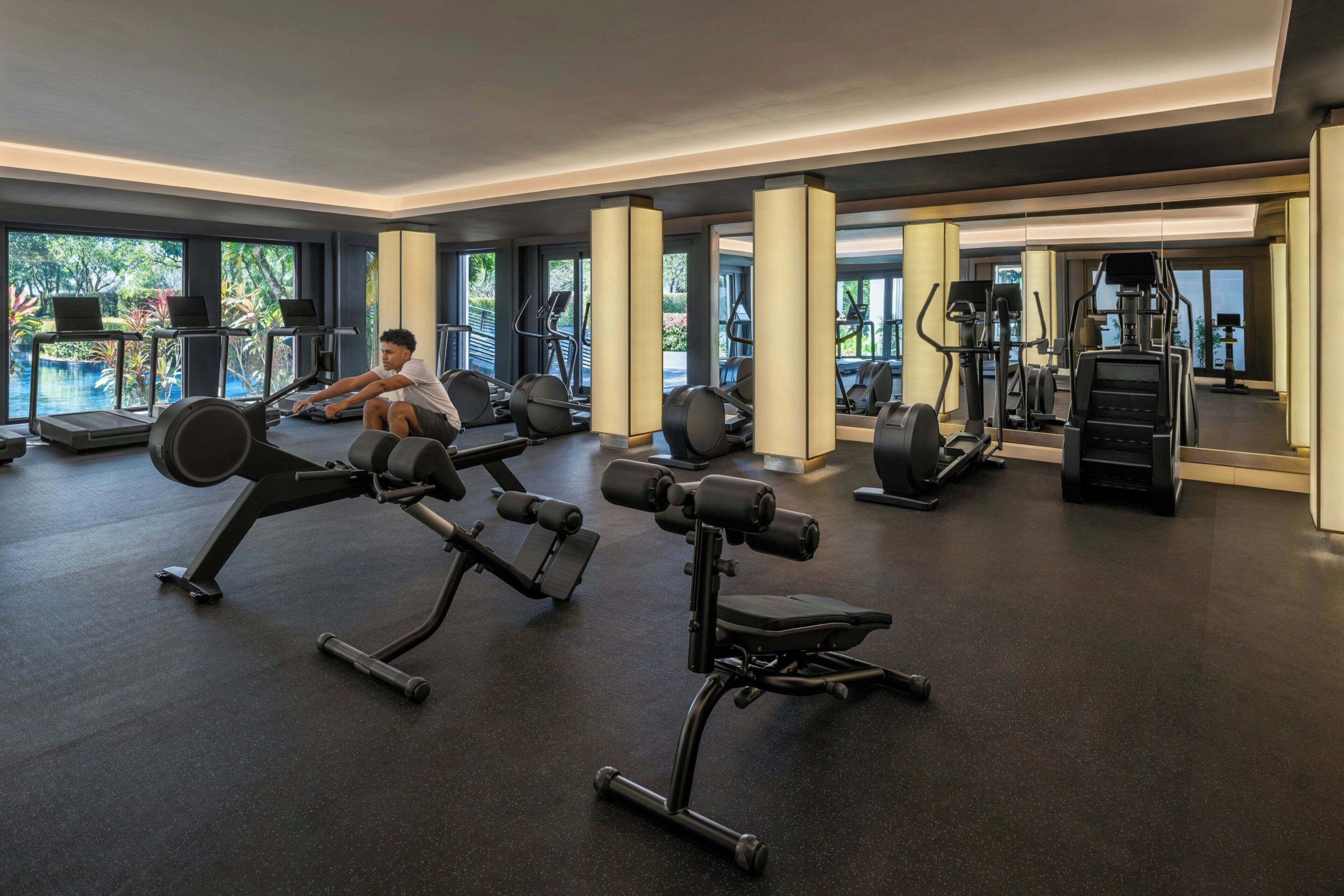 Un gimnasio con cintas de correr, máquinas de pesas y vistas a la piscina.