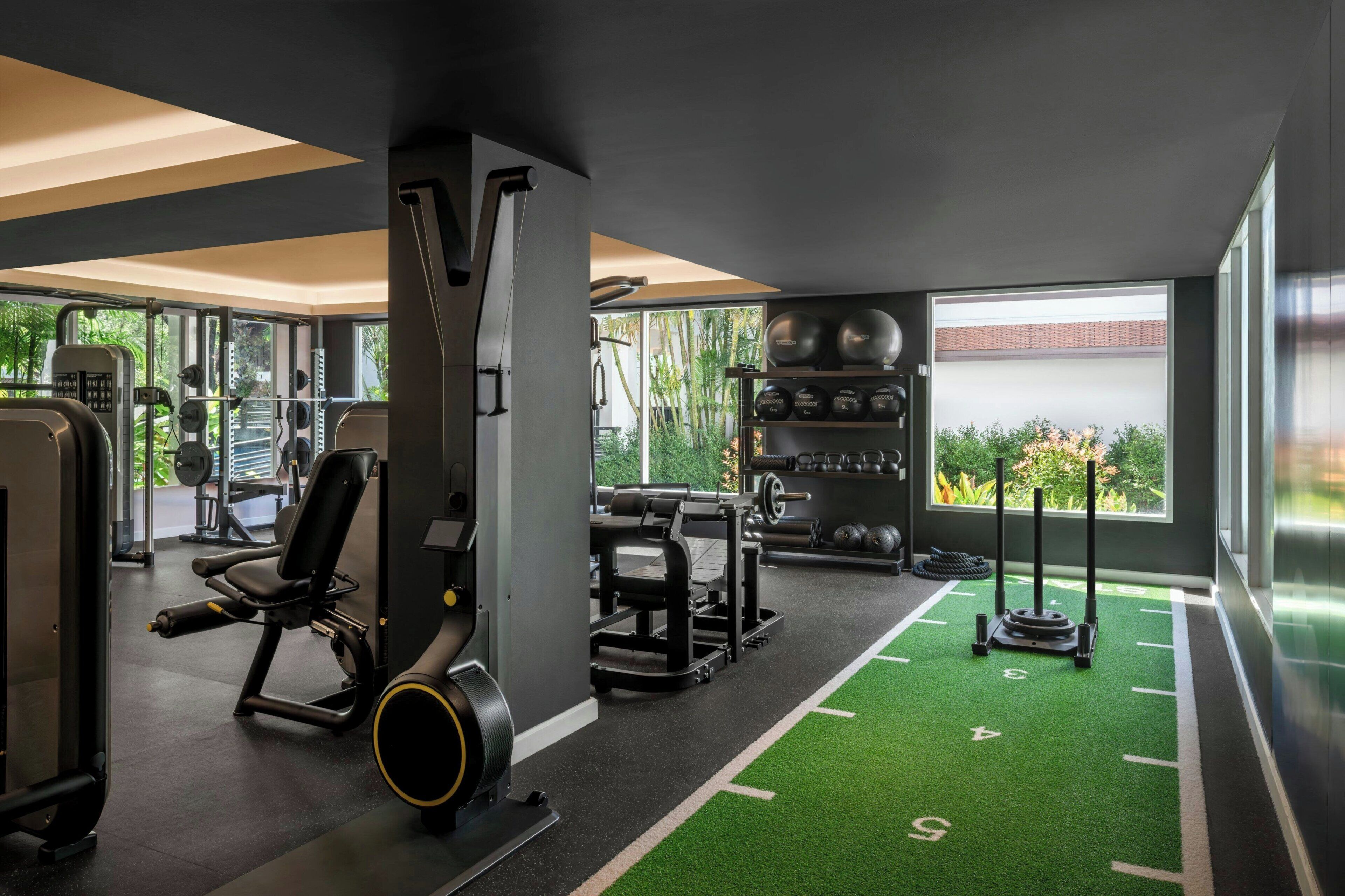 Ein Fitnessraum mit Trainingsgeräten, einer grünen Rasenfläche und großen Fenstern mit Blick ins Grüne.