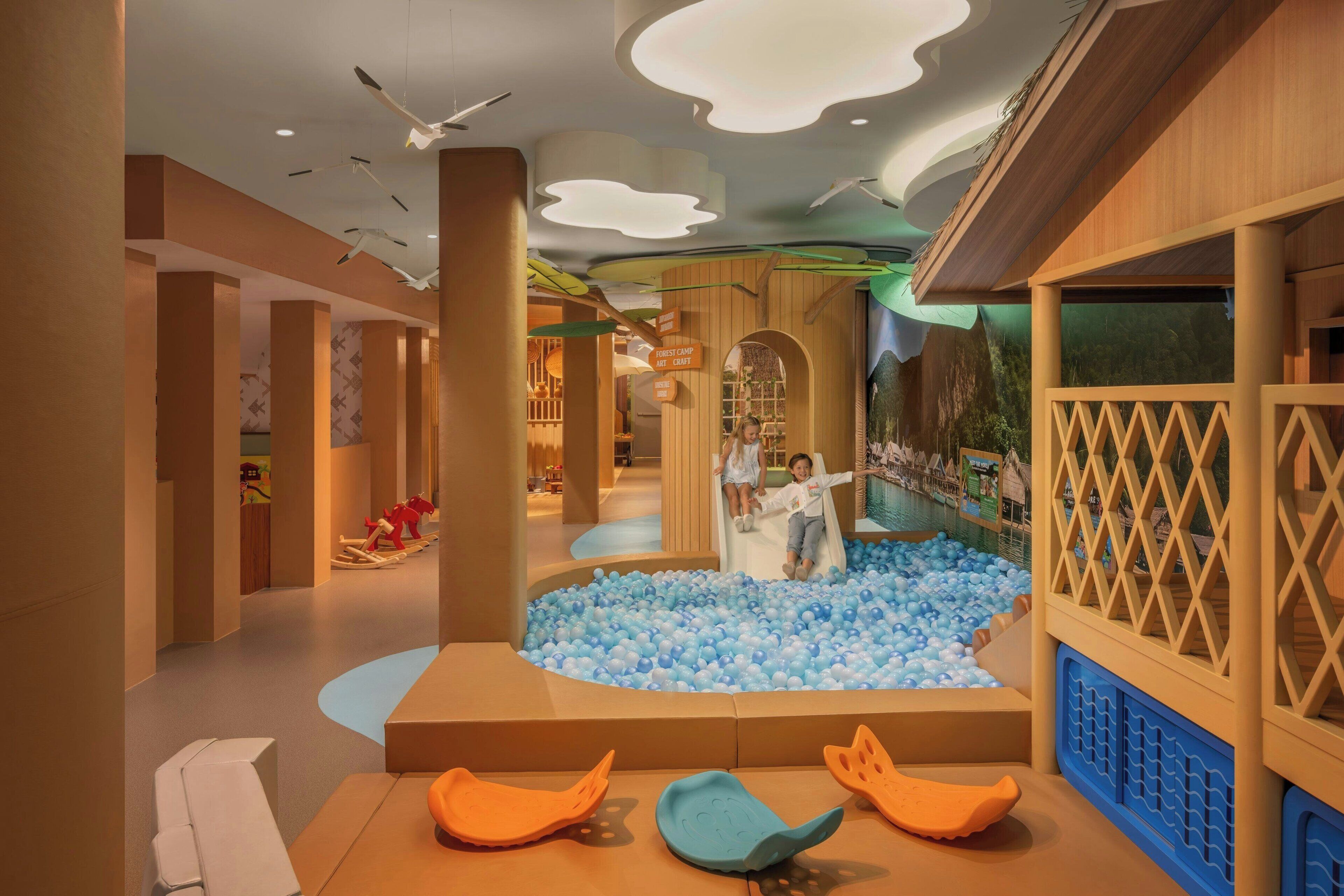 Zona de juegos infantiles con piscina de pelotas, toboganes y asientos acolchados.