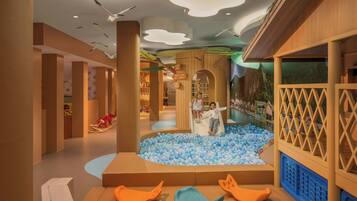 Zona de juegos infantiles con piscina de pelotas, toboganes y asientos acolchados.