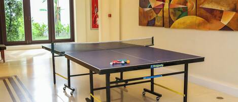 A ping pong table in a room with a large abstract painting on the wall and a view of greenery through the door.