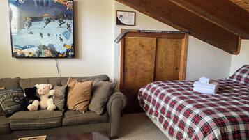 A cozy room with a striped couch, a bed with a plaid bedspread, a wooden wardrobe, a framed quote on the wall, and a painting of a snowy scene.