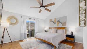 Ein Schlafzimmer mit einem Bett, einem Deckenventilator, einem großen Fenster mit Vorhängen, einer Stehlampe und einem Teppich.