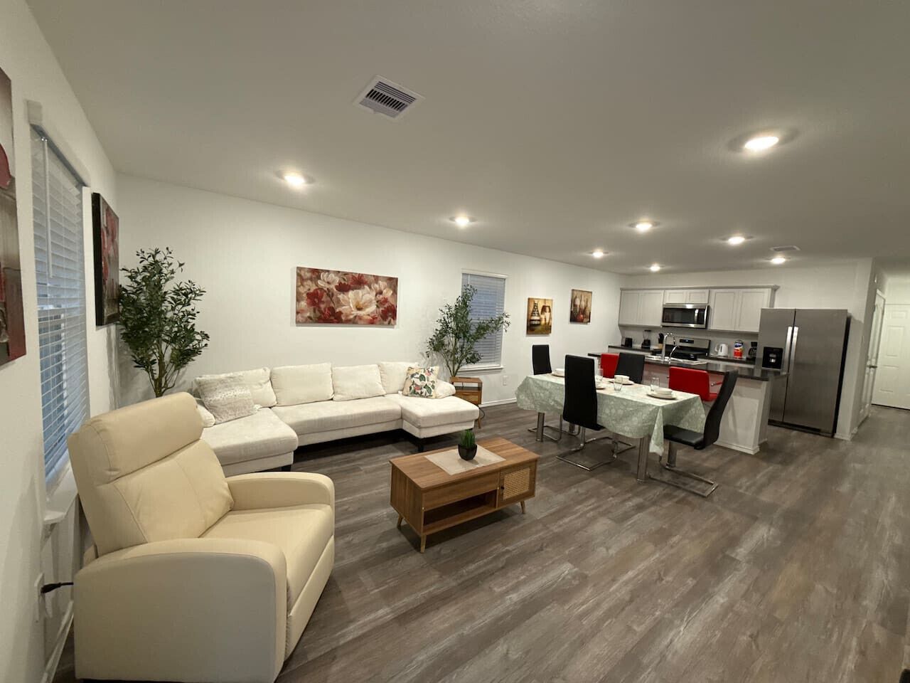 Ein modernes Wohnzimmer mit einer Eckcouch, einem Couchtisch und einem Essbereich mit Tisch und Stühlen. Es gibt eine Küchenzeile mit Kühlschrank, Mikrowelle und Herd.
