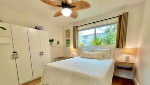 A bedroom with a bed, a ceiling fan, a window with curtains, a nightstand, and a wardrobe.