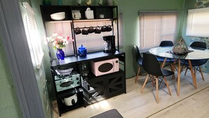 Una cocina compacta con comedor, que incluye un microondas, una cafetera y un estante con adornos.