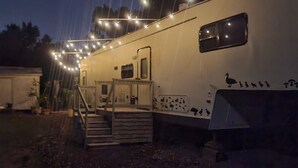 Una caravana estacionada con un porche cubierto, un juego de escalones y luces decorativas.