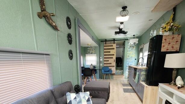 Una sala de estar con un sofá gris, una pequeña mesa de madera y una cocina con nevera y estufa.