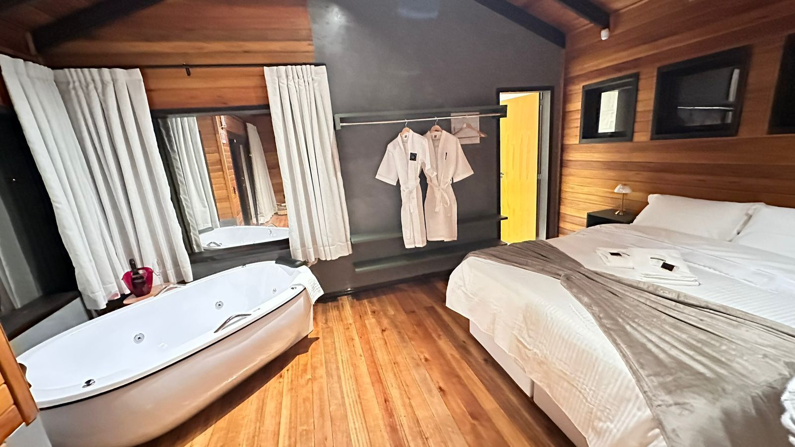 Una habitación con dos camas, piso de madera, bañera y un espejo.