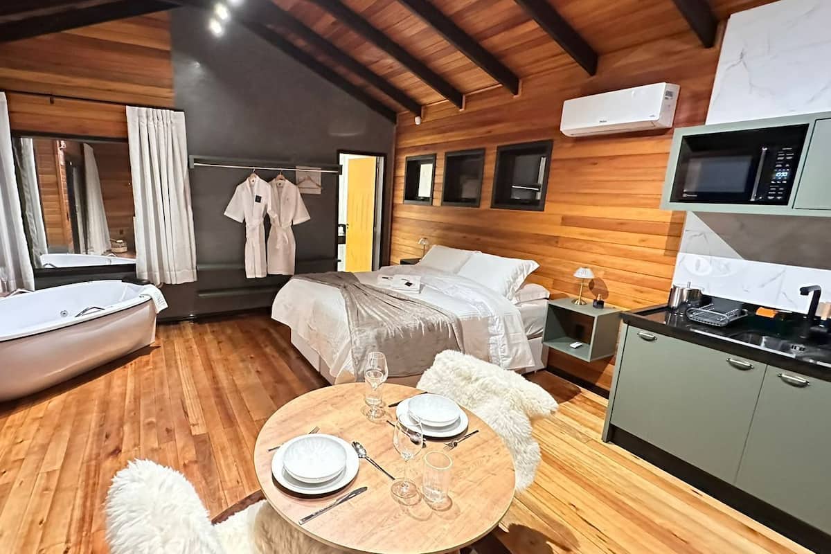Habitación compacta con cama, una mesa redonda para comer con sillas, una pequeña cocina con microondas y una bañera.