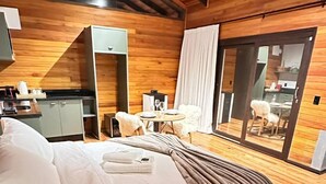 Quarto aconchegante com uma cama, uma mesinha, uma cadeira e vista através de uma porta de vidro.