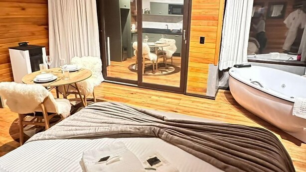Quarto de hotel com cama, mesa de jantar com cadeiras, pequena cozinha e porta de vidro deslizante que dá para um pátio externo.