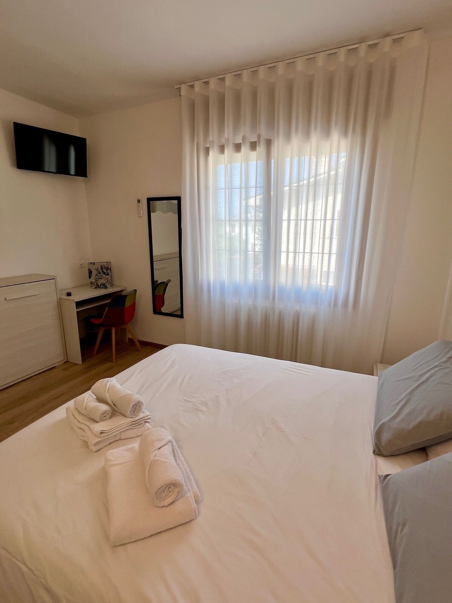 A hotel room with a bed, a desk, a chair, a mirror, and a window with curtains.