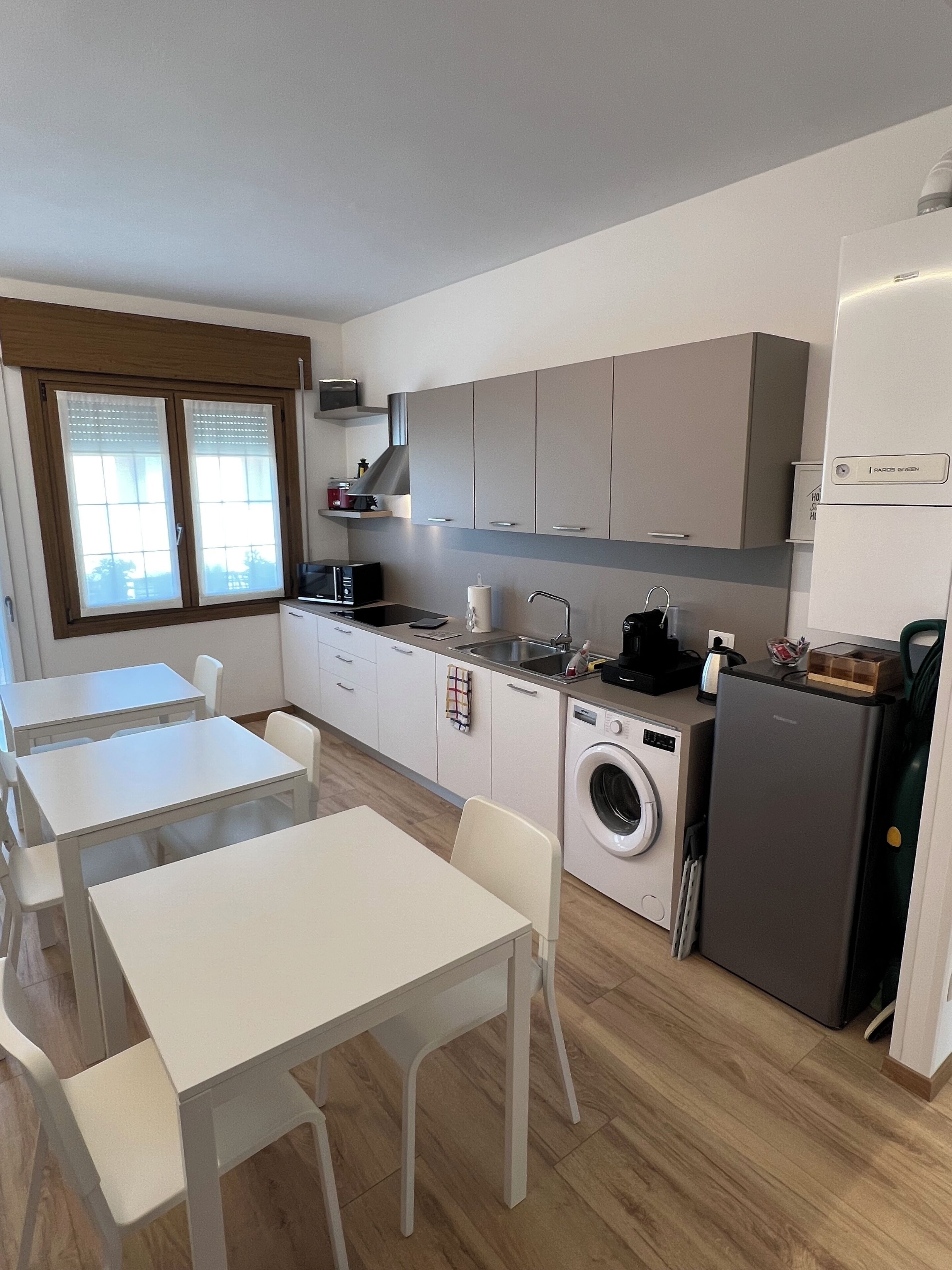 A compact kitchen with a washing machine, a refrigerator, and a dining area with white tables and chairs.