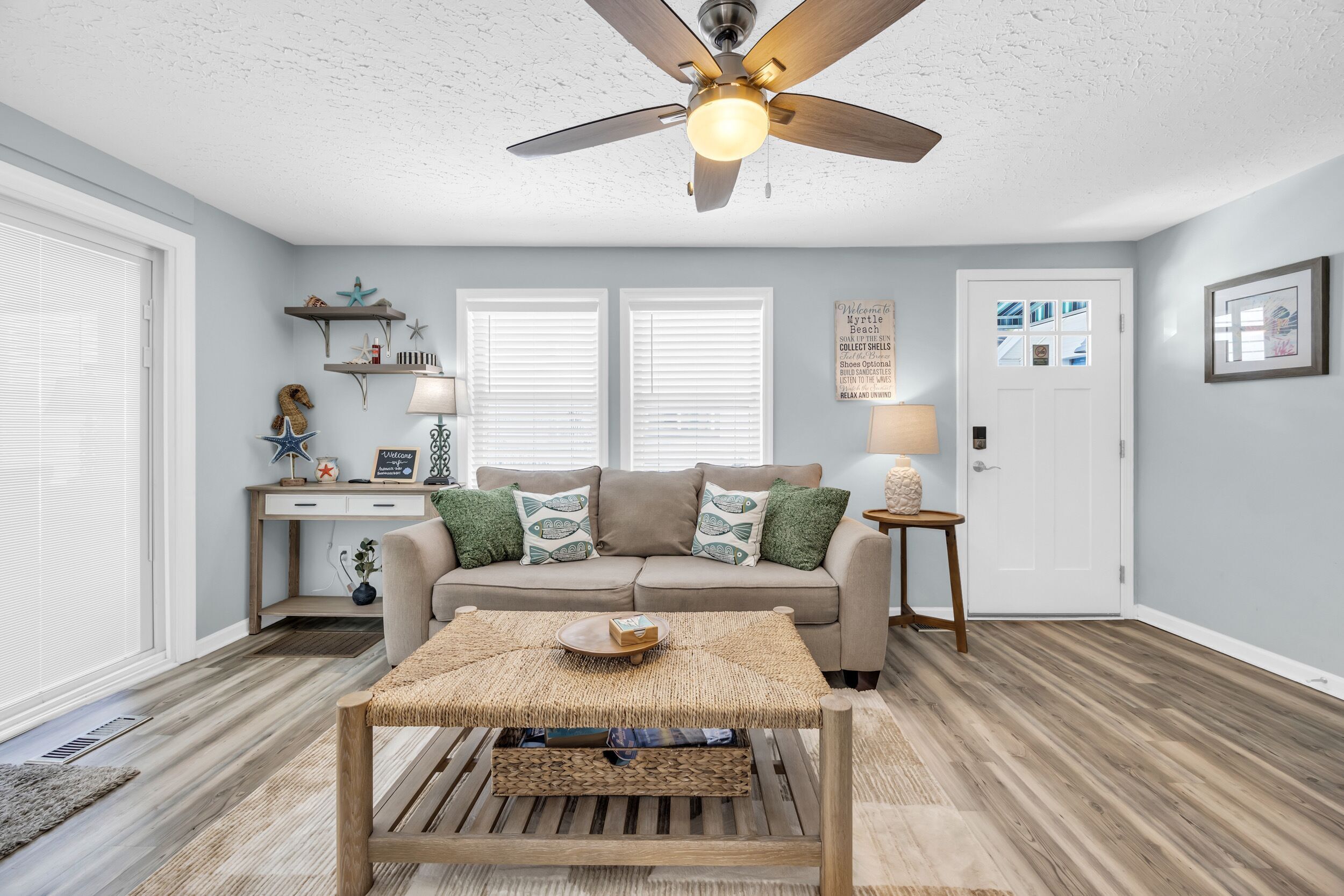 Sala de estar com ventilador de teto, sofá, mesa de centro e escrivaninha com luminária.