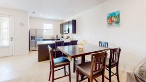 Una cocina moderna con una isla central, armarios oscuros y un comedor con mesa y sillas de madera.
