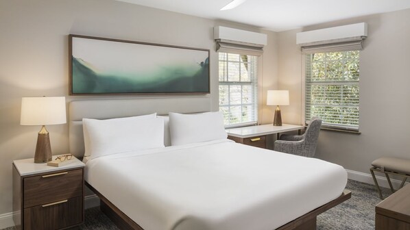 Habitación de hotel con una cama grande, dos mesitas de noche con lámparas, un escritorio, una silla y una ventana con persianas.