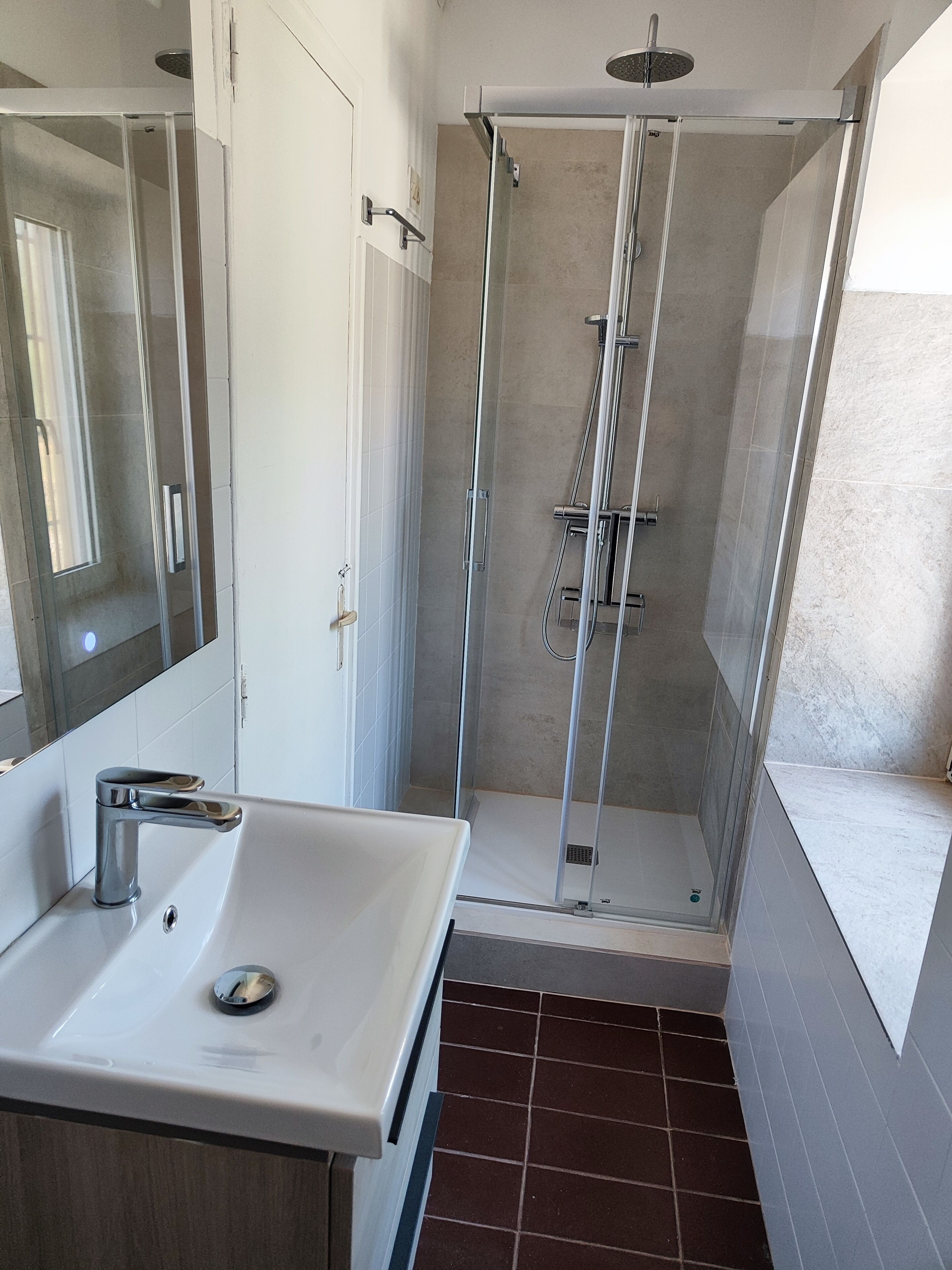 A modern bathroom with a glass-enclosed shower, a white sink, and a large mirror.