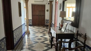 A hallway with a checkered floor, a wooden door, a table with chairs, and a mirror on the wall.