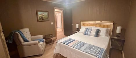 Een slaapkamer met een bed, een stoel, een nachtkastje en een plafondventilator.