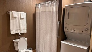 A bathroom with a toilet, a shower curtain, and a front-loading washing machine. - The Sandtown 3 bedroom Cabin (Vian)